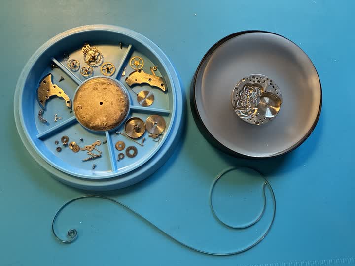 A vintage watch movement fully disassembled into a parts tray, mid-repair